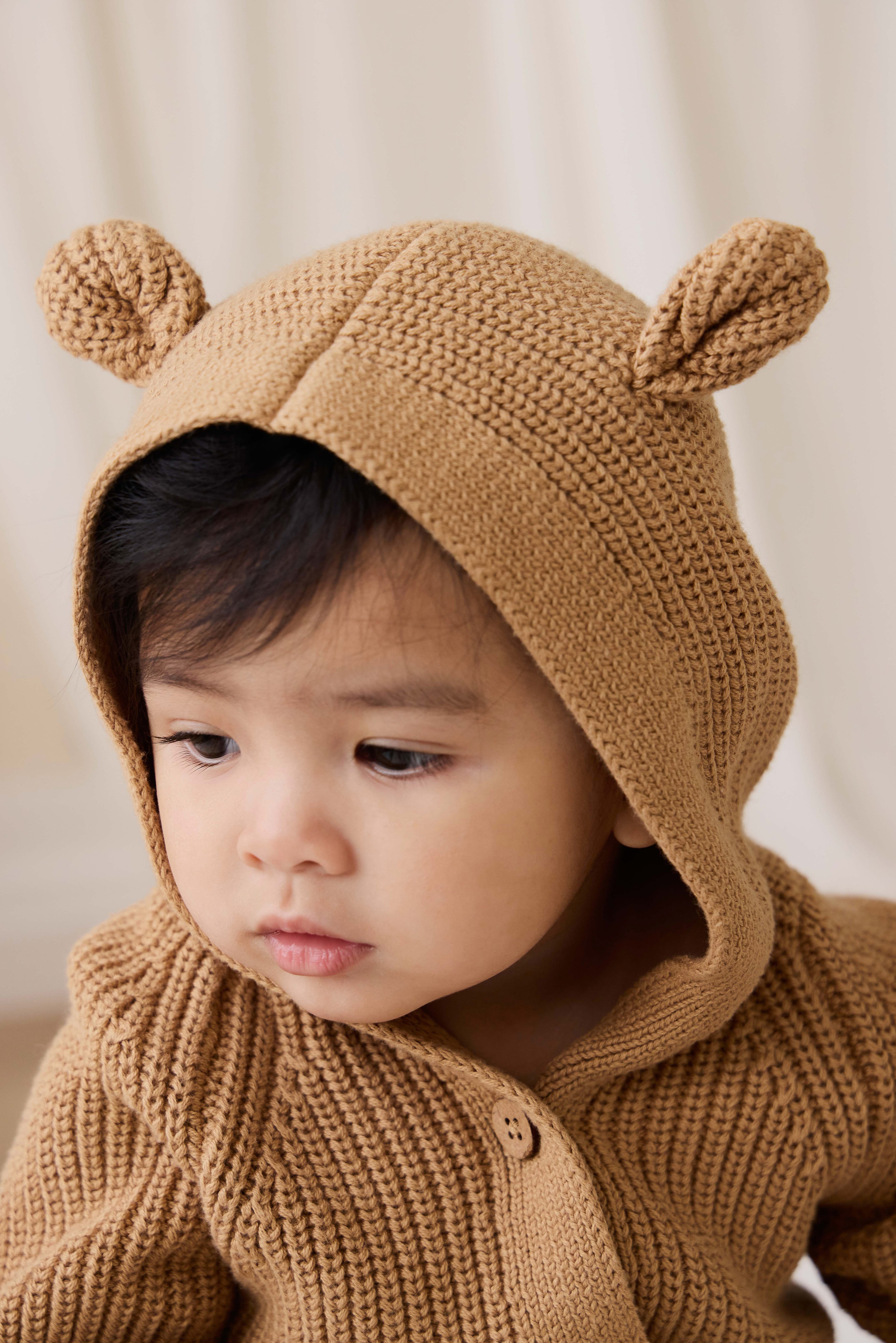 Grenouillère en tricot de coton douillet marron fauve avec capuche, oreilles et boutons sur le devant