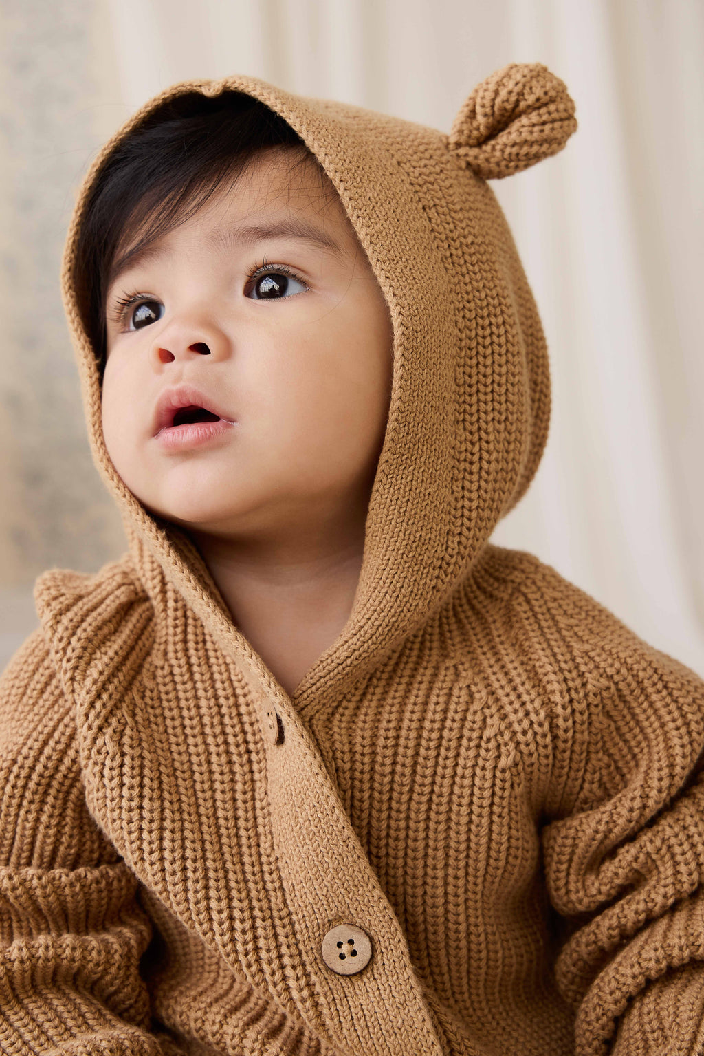 Grenouillère en tricot de coton douillet marron fauve avec capuche, oreilles et boutons sur le devant